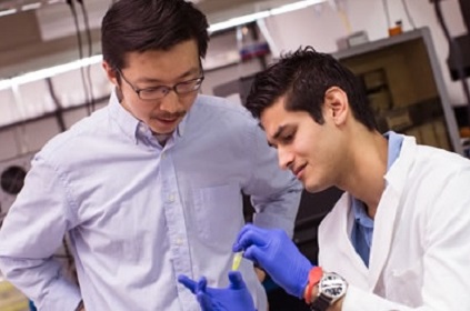 Jiou Wang looks on as a team member in a lab coat and blue gloves holds a plastic tube