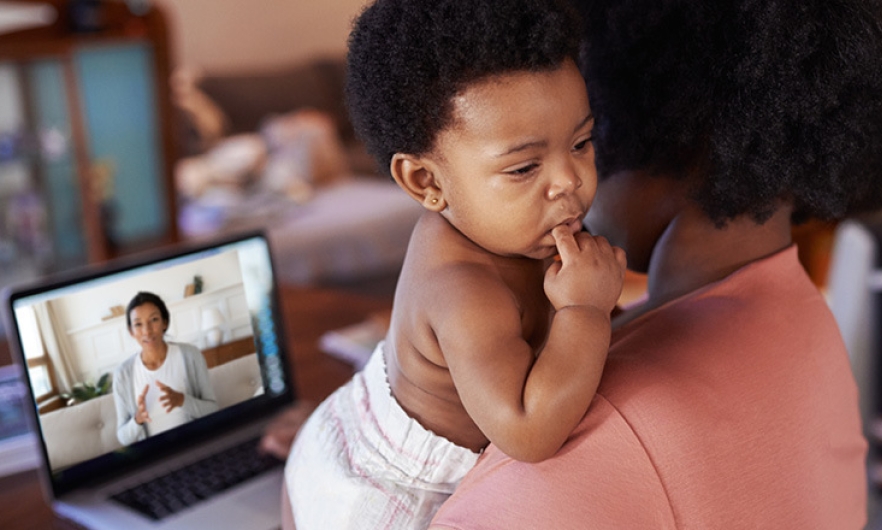 Woman holding a child while working on a computer