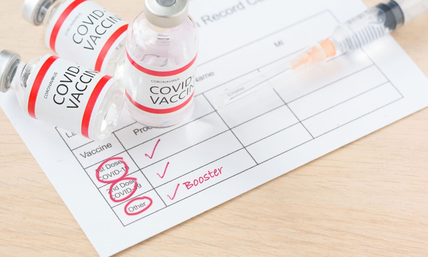 covid-19 vaccine vials and syringe laying on top of vaccine card