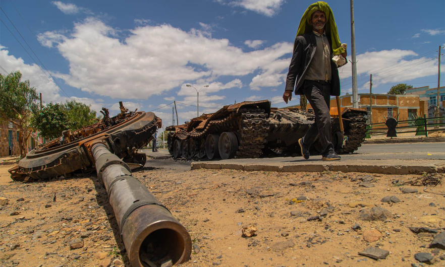 Elderly man walking past destroyed military tank