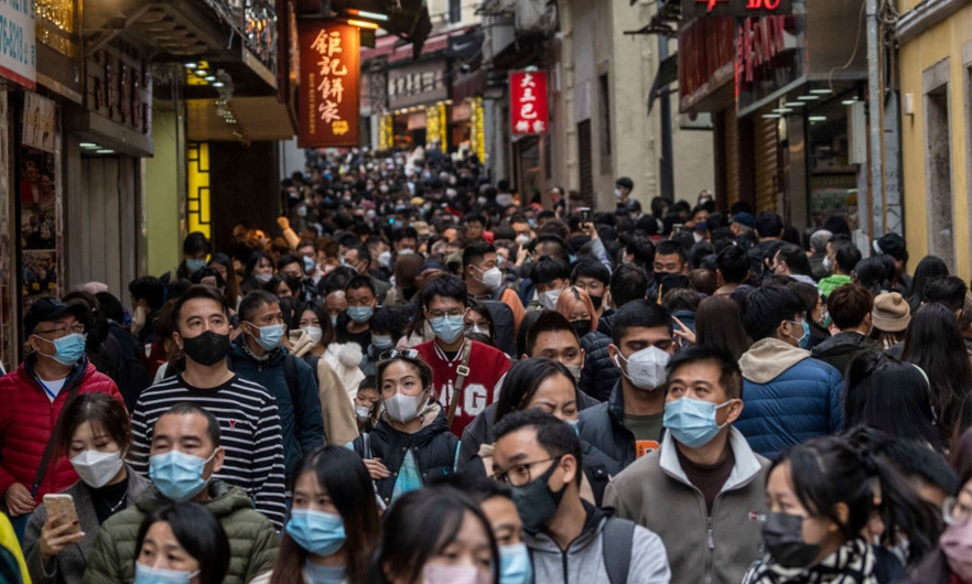 Large crowd of people wearing masks walking a narrow street in china 