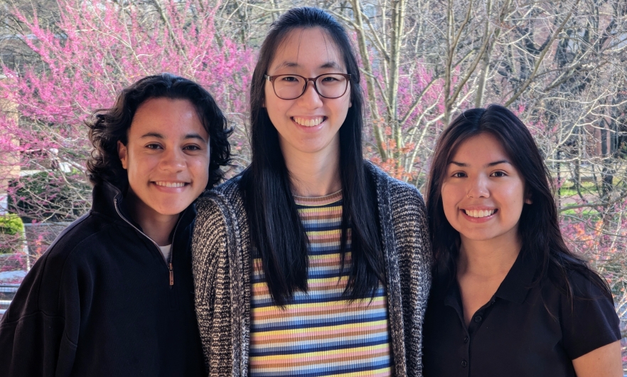 three young women posing in front of trees with pink blooms