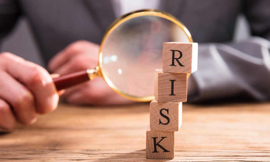 Close-up Of Wooden Blocks With Risk Word In Front Of Person's Hand Holding Magnifying Glass