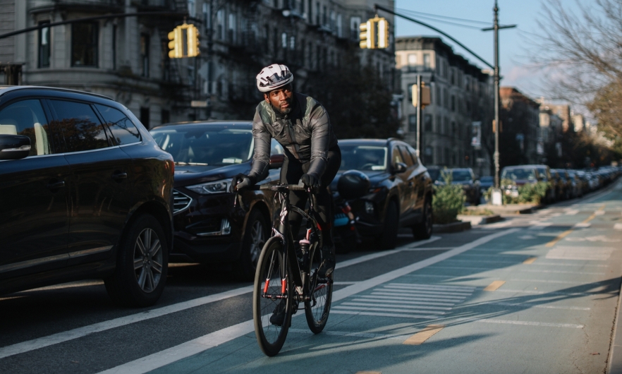 Person rides bicycle in the designated bike lane alongside a city street lined with cars