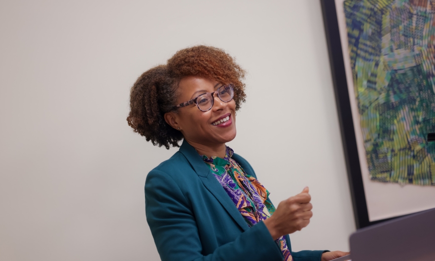 A female teacher standing behind a podium smiles at her classroom as she speaks.