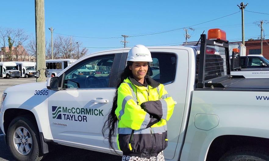 Woman in a hard hat and yellow vest standing in front of a white business truck