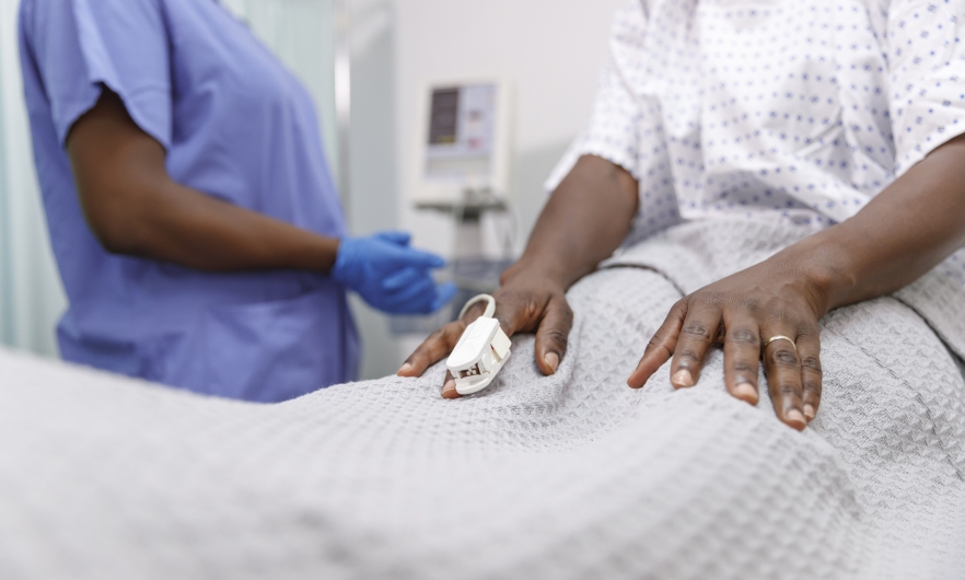 A nurse assists a patient on a hospital bed with a pulse oximeter