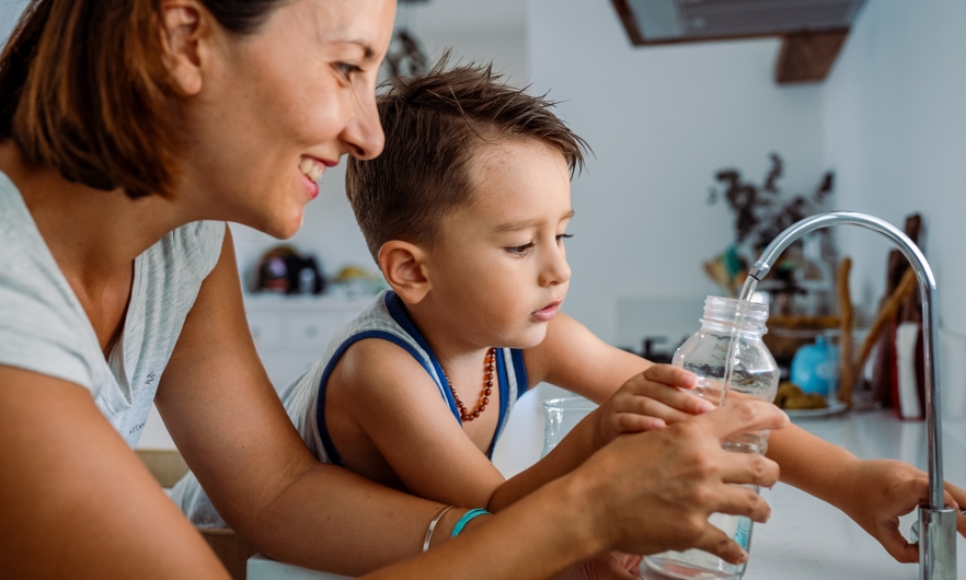 Mother and her toddler filling a glass with filtered water right from the sink's tap.