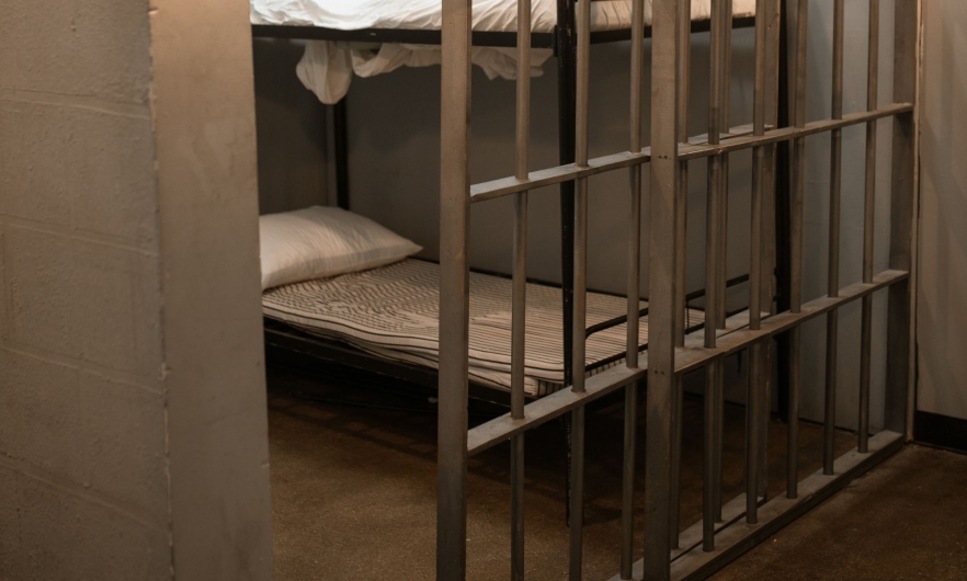 A jail cell with the bar doors opened halfway. A bunk bed is visible behind the bar door.