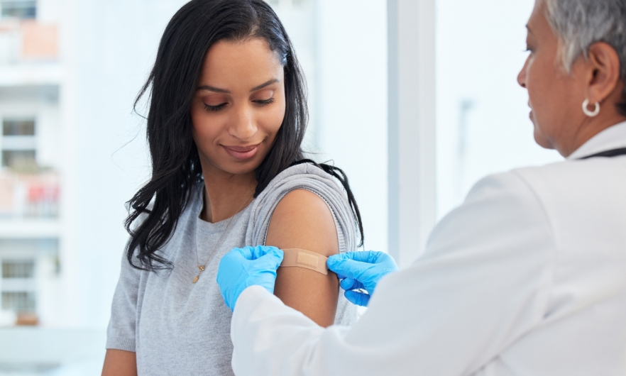 A doctor places a bandaid on a woman's upper arm following vaccination.