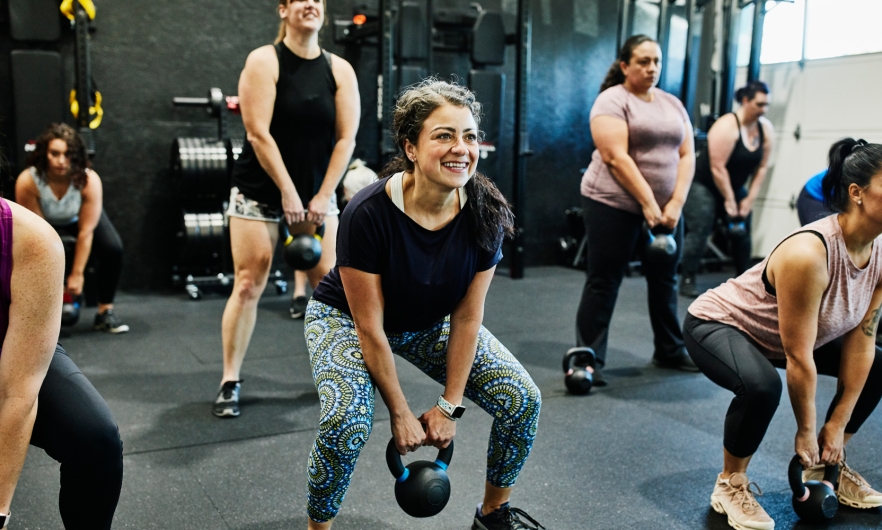 Smiling woman doing kettlebell swings while working out during class in gym