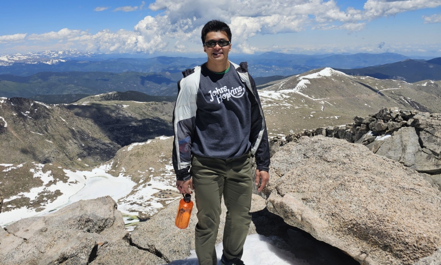 Young man standing on a rocky formation with a blue sky and white clouds in the background