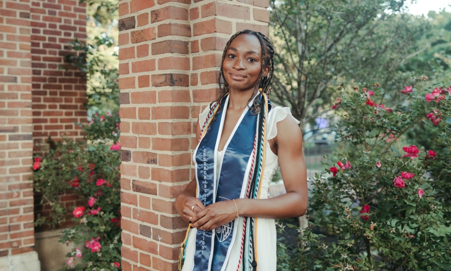 DMH_MHS_Pam Chiakpo Portrait of student against backdrop of brick columns and flower bushes