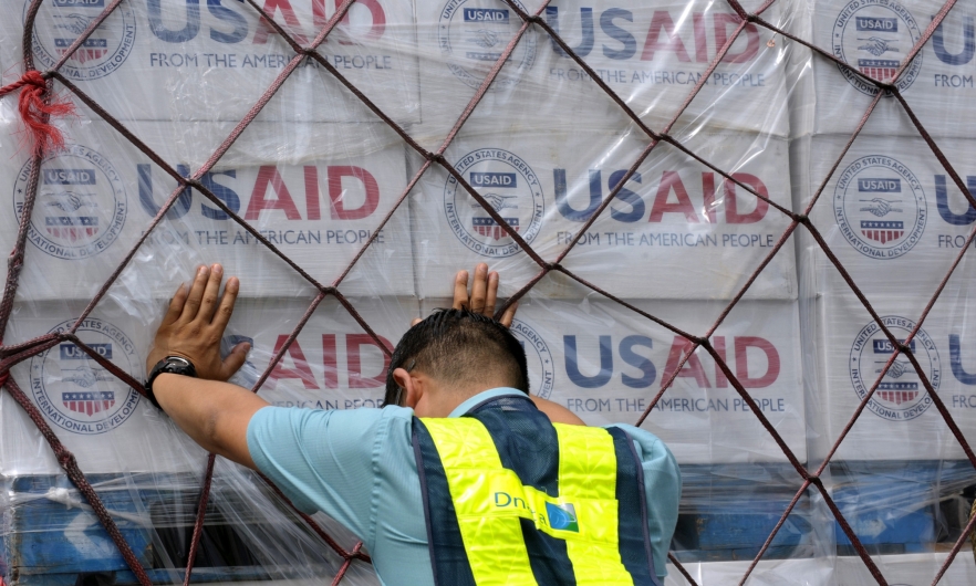 USAID supplies Worker pushes hands against a pallet stacked with boxes of USAID supplies