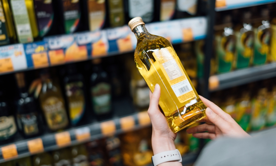 Cooking oil In front of shelves lined with various types of cooking oil, a shopper reads the label of a bottle of cooking oil.