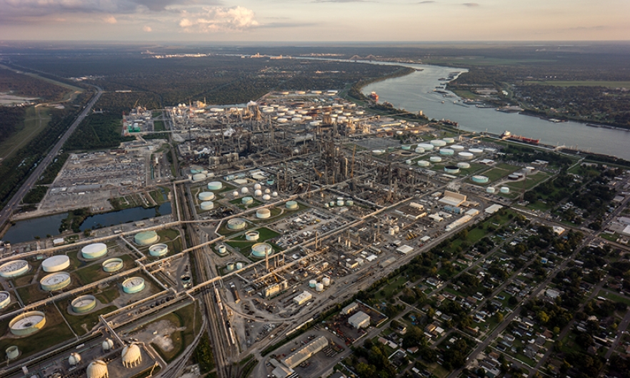 Aerial photo of a large area of petroleum processing plants bordered by residential communities. The Mississippi River snakes along to the east.