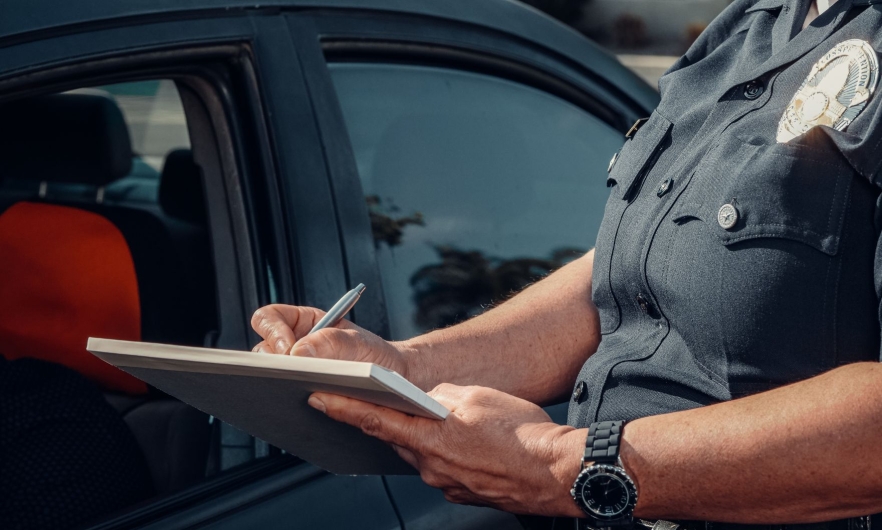 A police officer writing on a notepad next to a car.