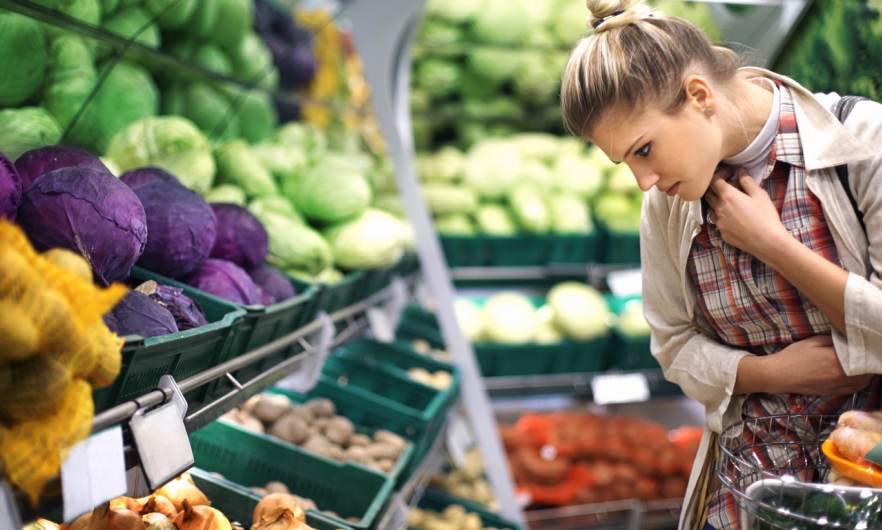 A woman looks at options in a produce section that includes red and green cabbages, onions, tomatoes, and more