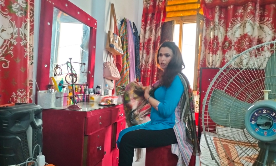 Photo of a transgender person in Pakistan, seated at a vanity with a fan in the foreground.