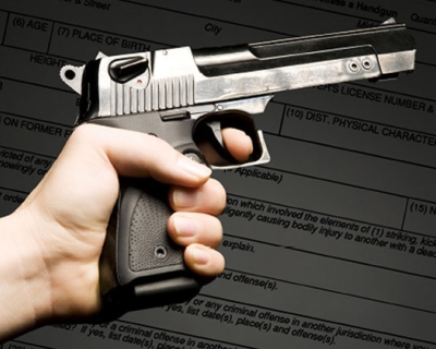 A gun held in hand superimposed over a sample permit form