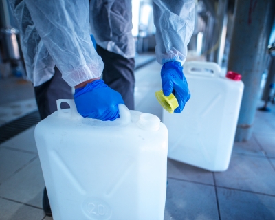 worker in protective clothing and gloves carrying two containers with chemicals