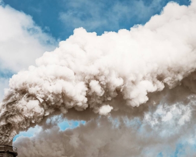 smokestack spewing smoke into a blue sky with clouds