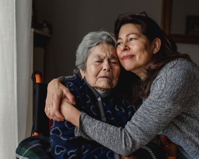 caregiver/daughter hugging elderly parent in wheelchair