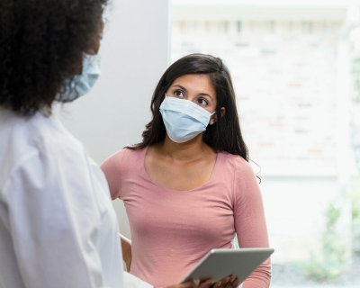 A female patient listening to a female doctor, who is showing her information on a digital tablet