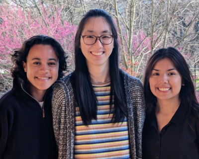 three young women posing in front of trees with pink blooms