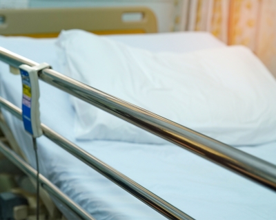 an unoccupied hospital bed with a white sheet; the side guard rail us up