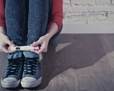 A teenager holds a positive pregnant test while sitting on the ground.