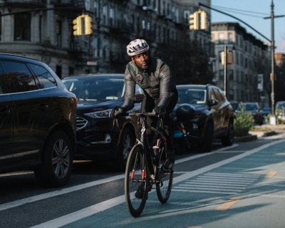 Person rides bicycle in the designated bike lane alongside a city street lined with cars