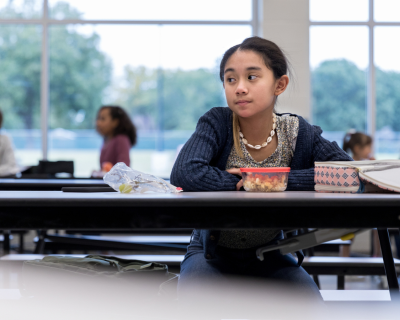 A girl sits alone in a school cafeteria with little to no food for lunch