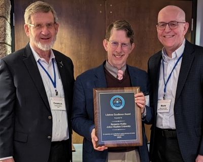 three men posing for a photo, with the center man holding an award