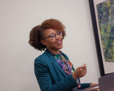 A female teacher standing behind a podium smiles at her classroom as she speaks.