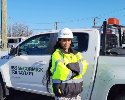 Woman in a hard hat and yellow vest standing in front of a white business truck