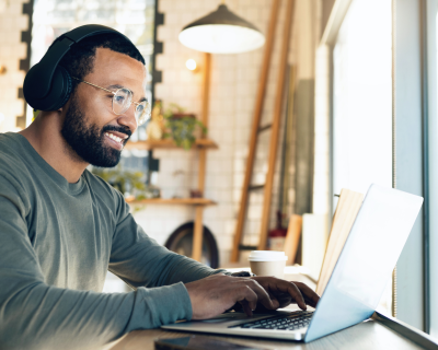 Man wearing headphones and smiling while working on laptop