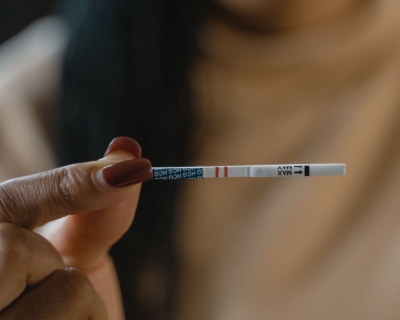 A hand holding a fentanyl test strip. Two short red lines run down the middle of the test strip.