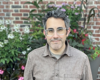 man wearing glasses standing outside with flowers in the background