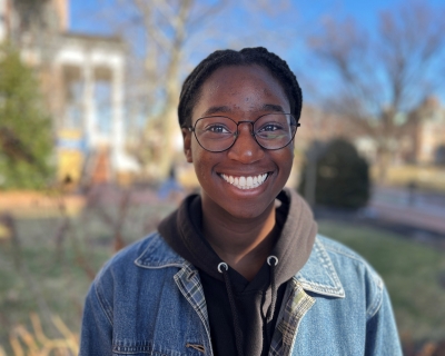 Head shot of a young black woman with buildings and trees in the background