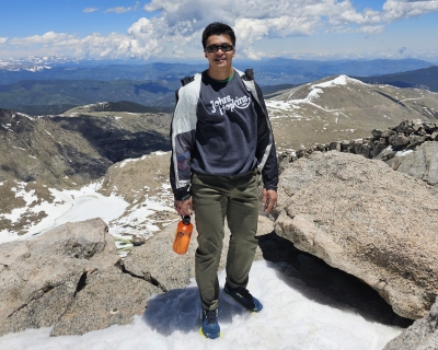 Young man standing on a rocky formation with a blue sky and white clouds in the background
