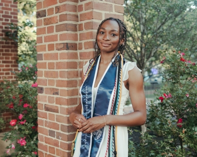 Portrait of student against backdrop of brick columns and flower bushes