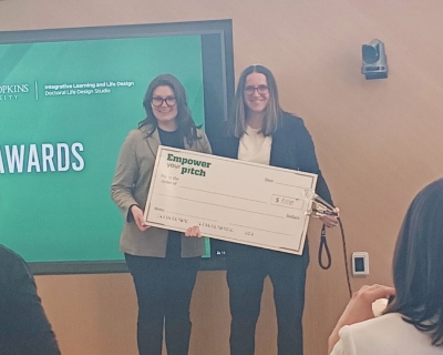 Two women stand on stage holding a giant check