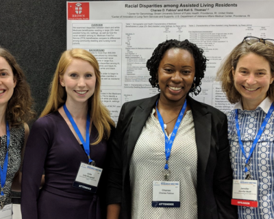 Four women standing side by side in front of presentation poster