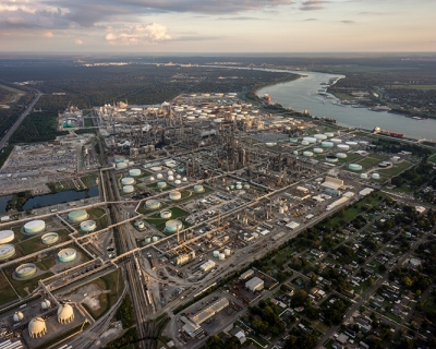 Aerial photo of a large area of petroleum processing plants bordered by residential communities. The Mississippi River snakes along to the east.