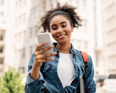 Teenager using smartphone Teenager smiling while holding smartphone outside