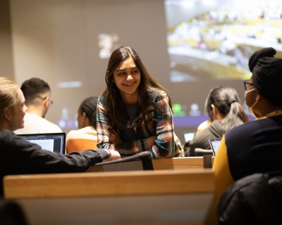 three students chat before class in a lecture hall set up for hybrid learning