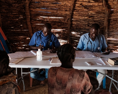 Two doctors sitting at a table consult with patients  in a clinic a camp for internally displaced persons.