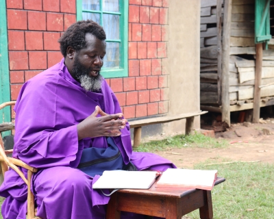  Eliud Wekesa, hands clasped, with a graying beard and wearing a bright purple robe, speaks to visitors outside his home and church compound in Tongaren, Bungoma County, Kenya, on February 29, 2024.
