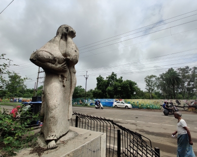 A statue of a mother holding her child with her hand over her face, against a cloudy grey sky. 